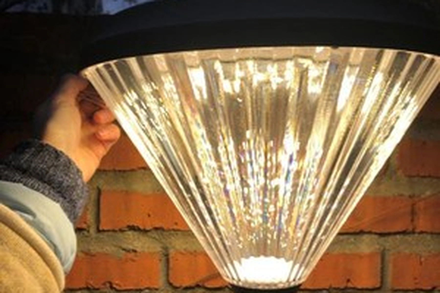 SWL-4005 diamond wall sconce casting brilliant prismatic light on brick wall at dusk